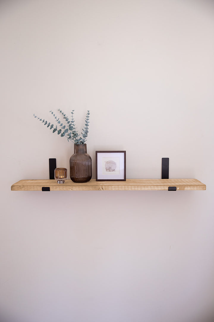 Houten wandplank in de kleur lichtbruin bevestigd met zwarte stalen beugels aan de muur